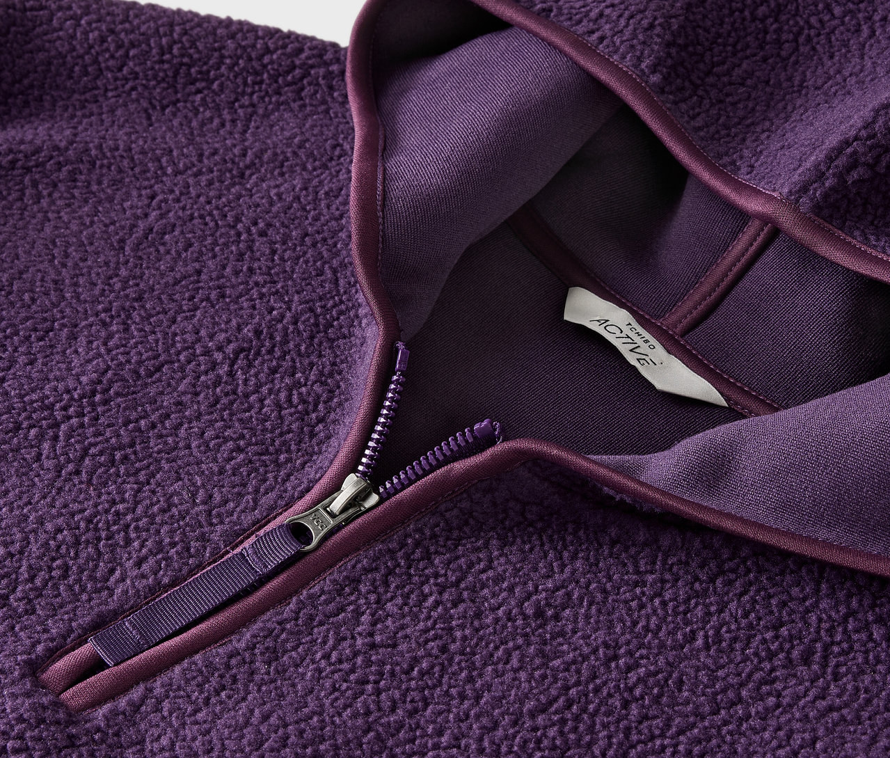 Fermuarlı ve etiketli mor polar sweatshirt'ün yakın çekimi.
