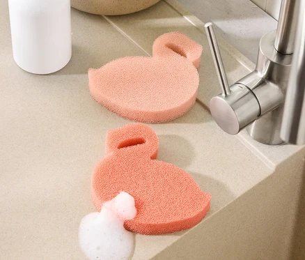 Lavabonun yanındaki tezgahta iki adet flamingo şeklinde silikon sünger duruyor, birinin üzeri köpükle kaplı.
