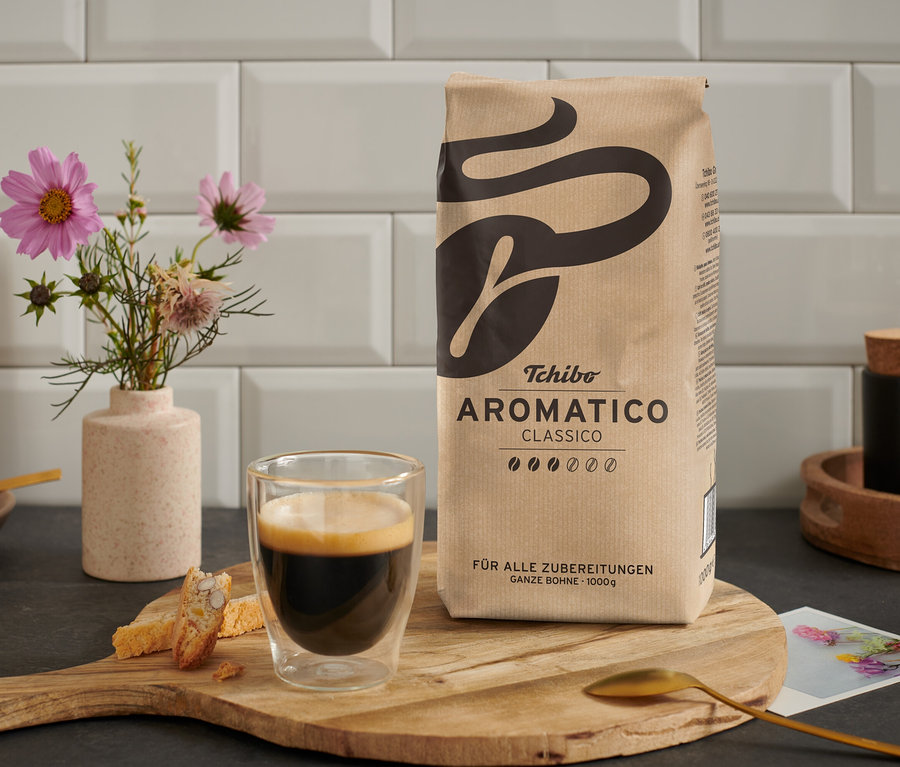 Bir fincan kahve, ahşap bir masanın üzerinde bir paket Aromatico Classico - 1 kg Ganze Bohne yanında duruyor.