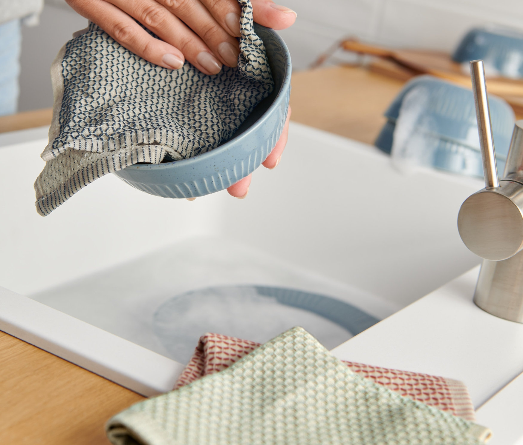 Kadın, lavabonun yanında 3 Adet Organik Pamuklu Bulaşık Bezi ile mavi bir kaseyi siliyor.