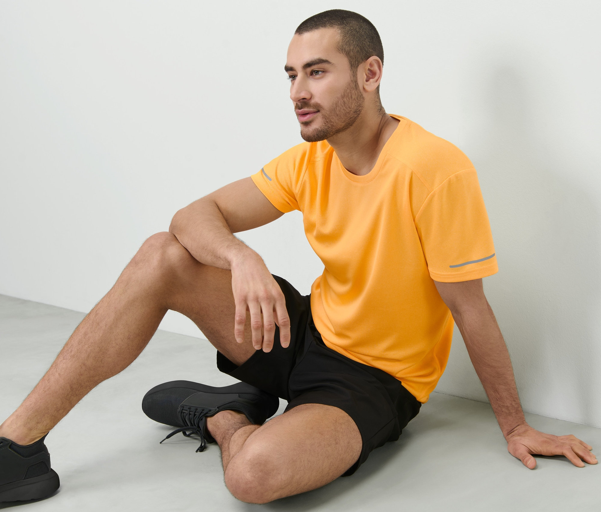 Adam yerde oturuyor ve şeftali rengi fonksiyonel tişört giyiyor.