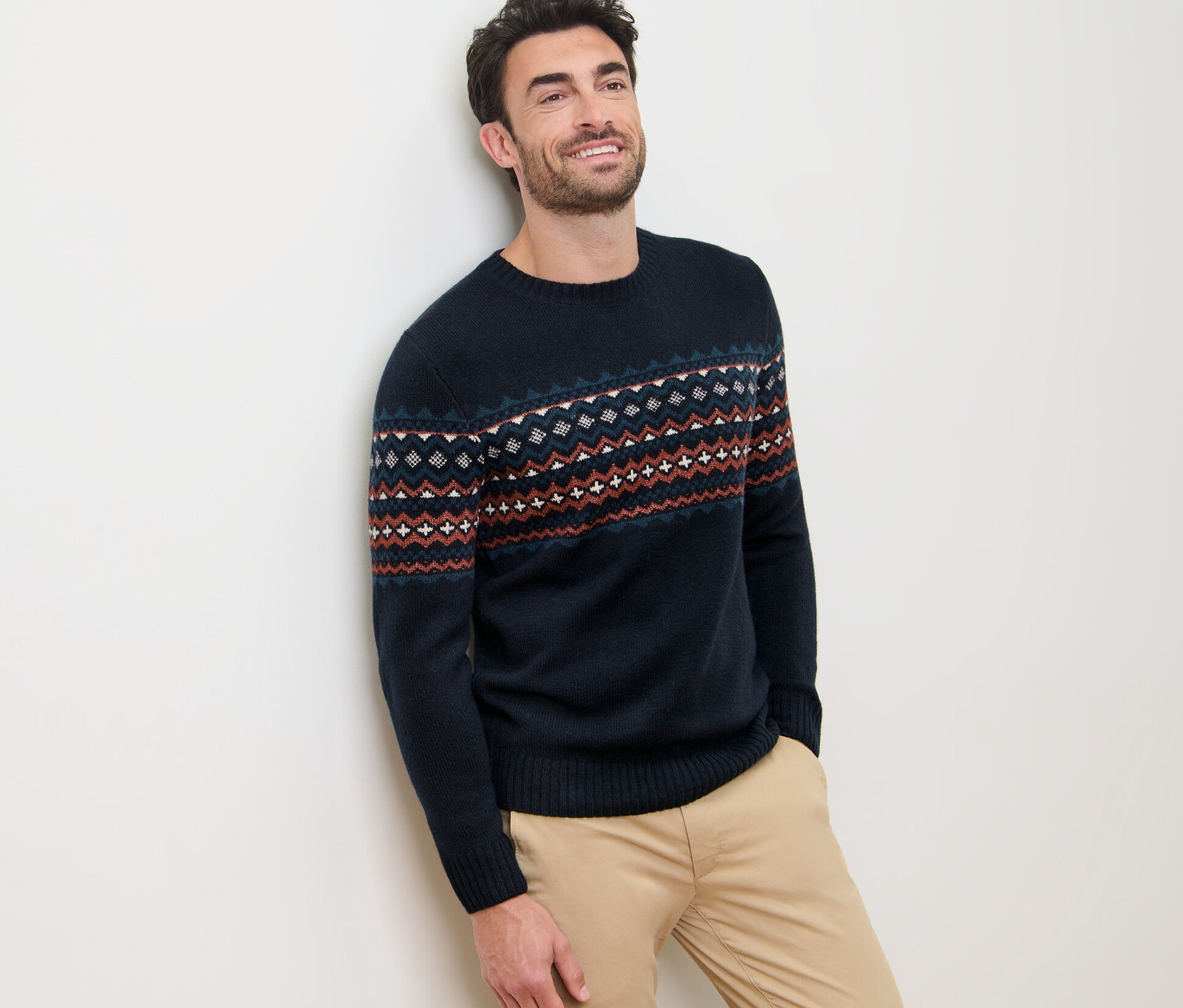 Duvara yaslanmış, üzerinde örgü kazak olan bir adam.