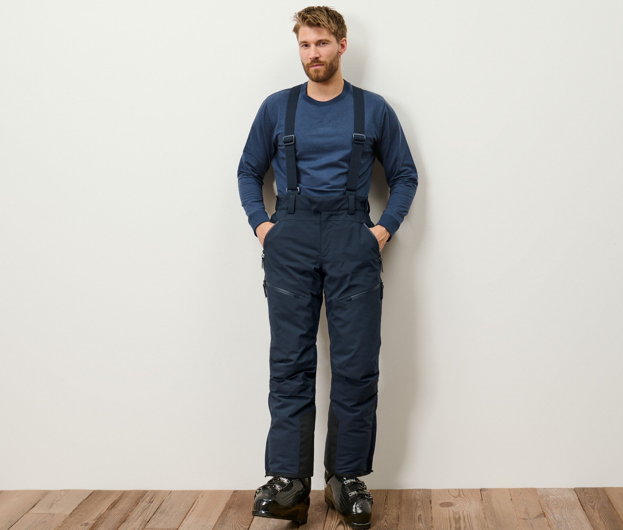 Adam ayakta duruyor ve mavi Yüksek Teknolojili Kayak Pantolonu giyiyor.