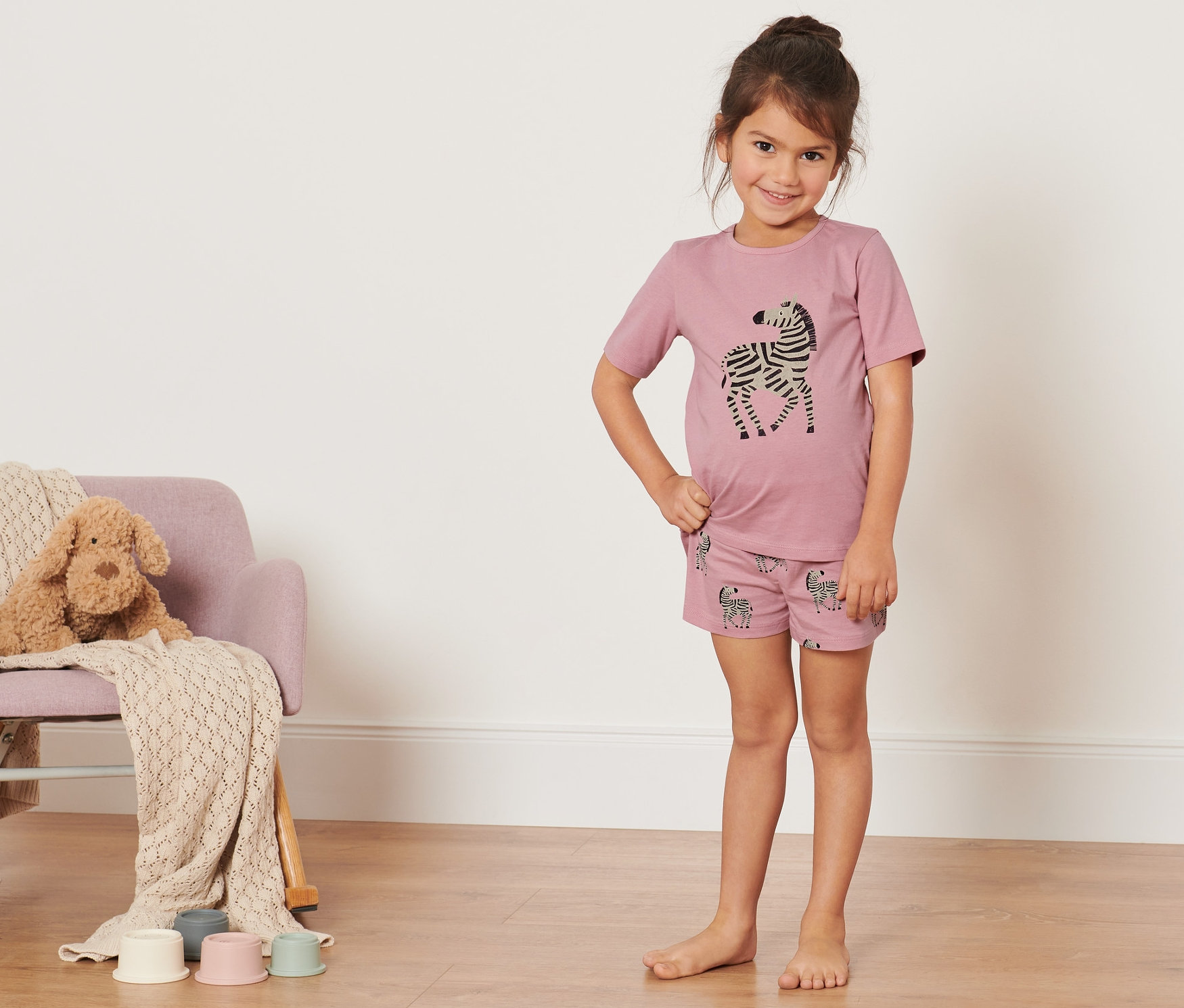 Gülümseyen kız çocuğu zebra desenli çocuk şortlu pijama takımıyla poz veriyor.