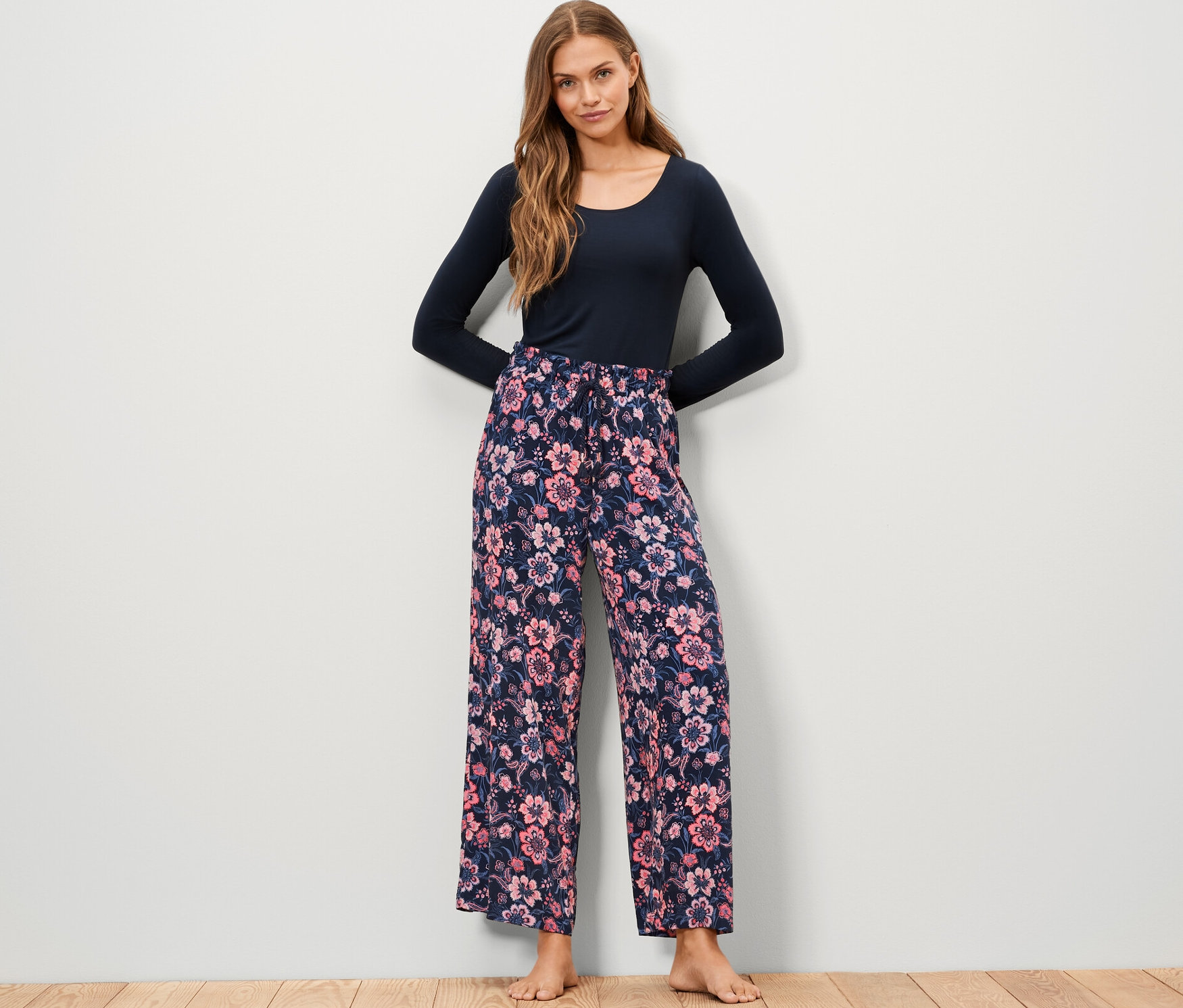 Bir kadın çiçek desenli dokuma rahat pantolon ve uzun kollu mavi bir bluz giyiyor.