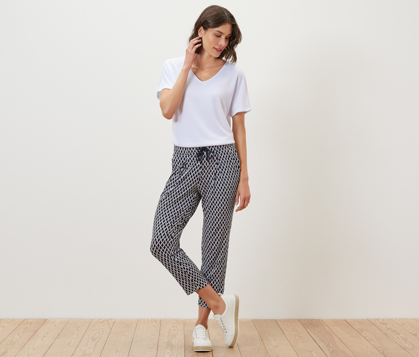 Kadın beyaz tişört ve baskılı jersey pantolonla poz veriyor.