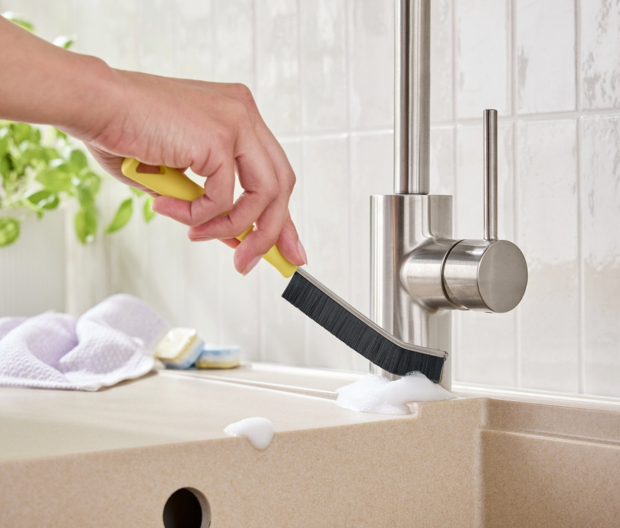 Bir el lavabodaki musluğu sarı bir fırçayla temizliyor.