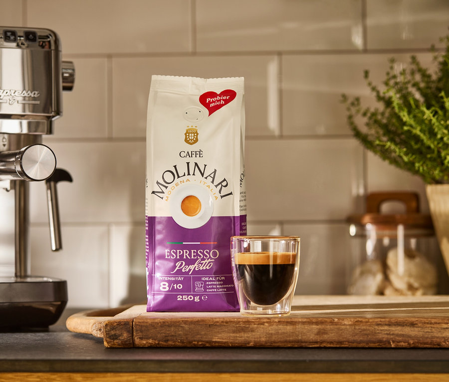 Gümüş renkli »Lapressa« Portafiltre Makinesi, bir paket Caffè Molinari ve tahta bir tahtada bir fincan espresso.