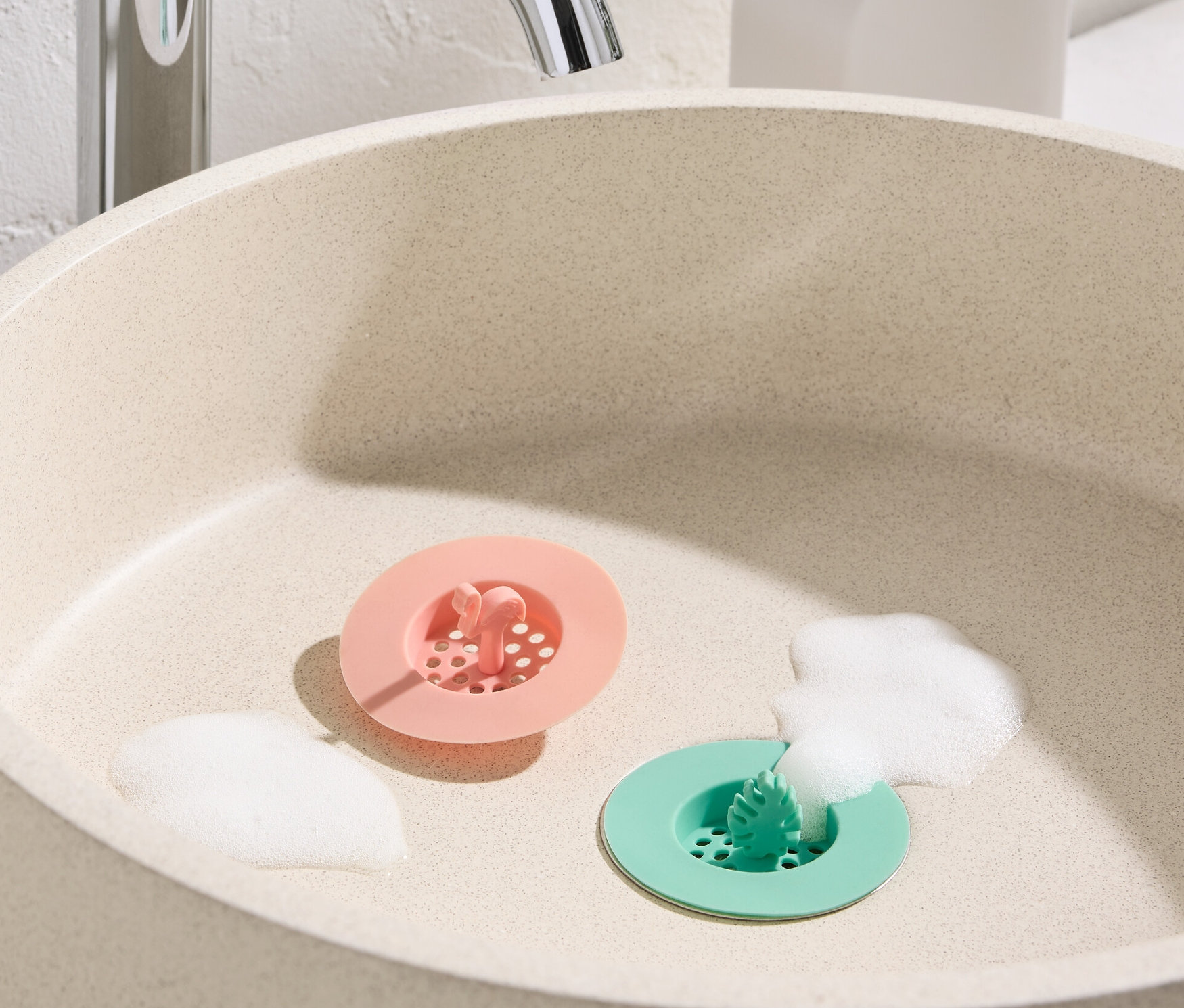 Lavabo pembe ve yeşil 2 silikon lavabo süzgeci ve köpük ile birlikte duruyor.