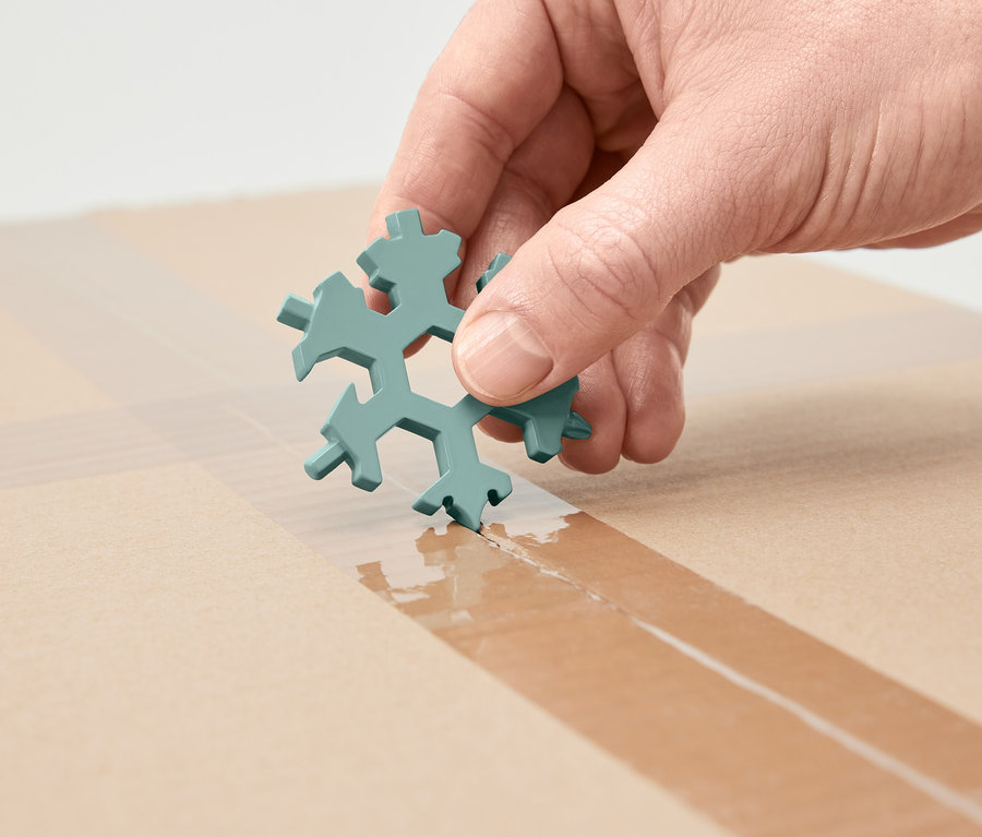 Bir el, kar tanesi şeklinde çok fonksiyonlu bir anahtar tutuyor ve onunla bir karton üzerindeki yapışkan bandı kesiyor.