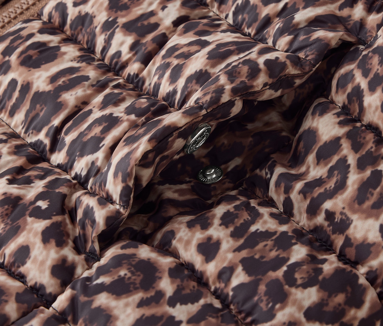 Hayvan deseni ve gümüş çıtçıtları olan kahverengi kapitone bir ceketin detayı.