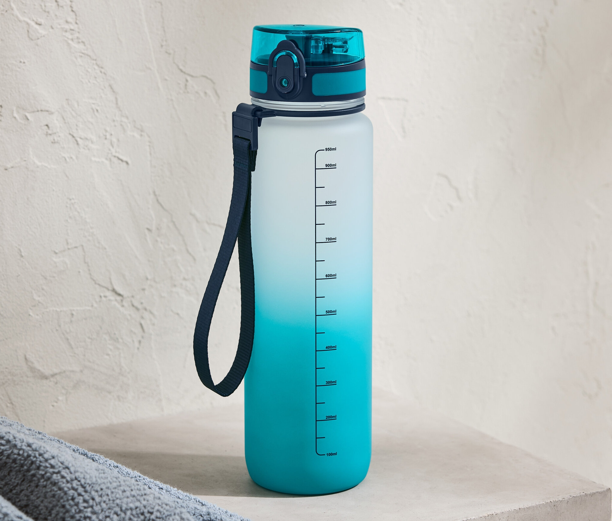 Mavi renk geçişli matara beton bir raf üzerinde duruyor.