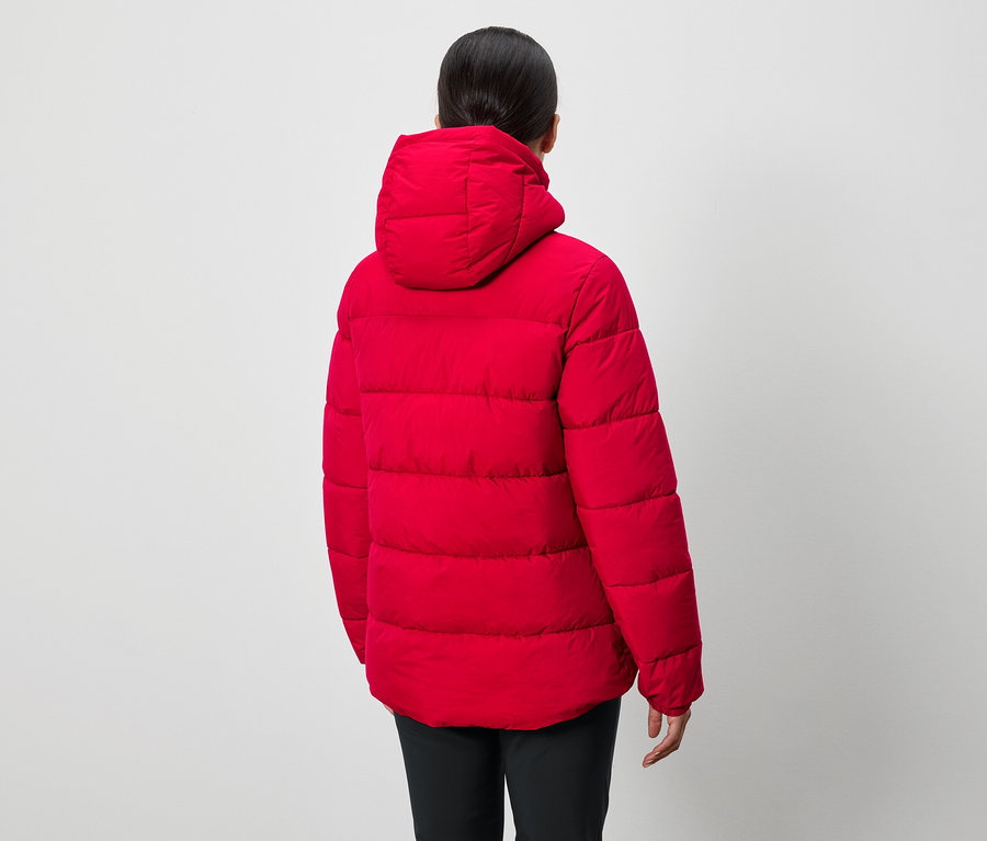 Kameraya arkası dönük bir kişi kapüşonlu kırmızı bir şişme mont ve siyah pantolon giyiyor.