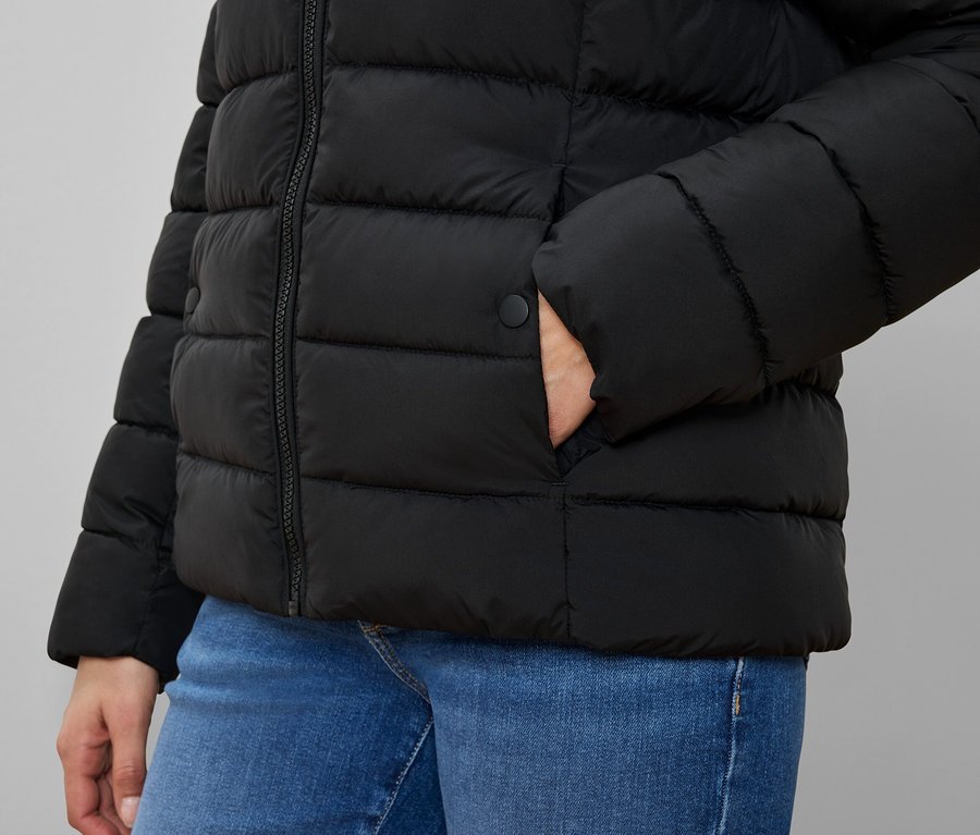 Cebinde eli olan siyah şişme montlu ve mavi kot pantolonlu kişi.