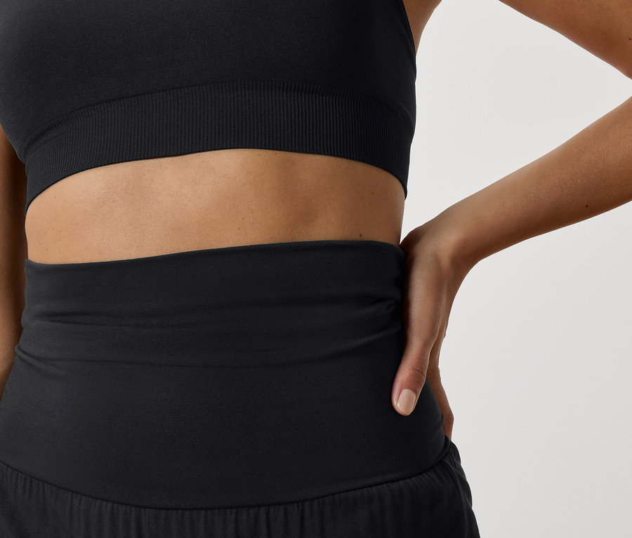 Siyah sporcu sütyeni ve siyah spor şortu giyen bir kadının detayı.