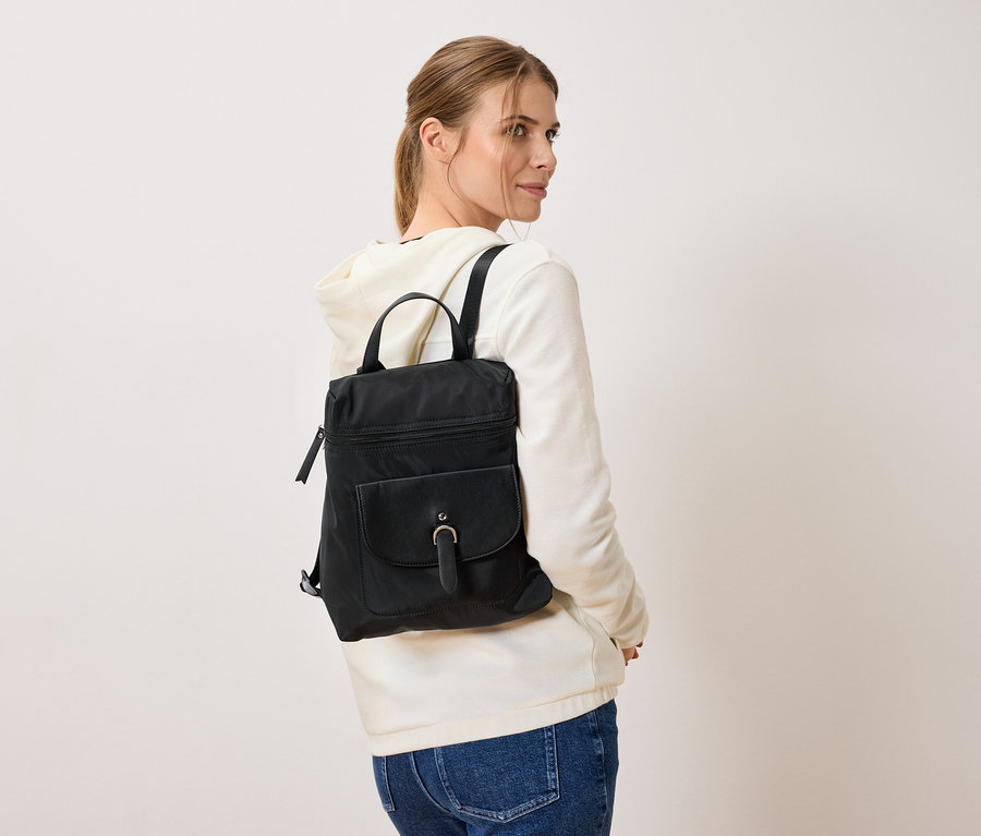 Beyaz bir arka plan önünde duran, sırtında siyah bir sırt çantası olan kadın.