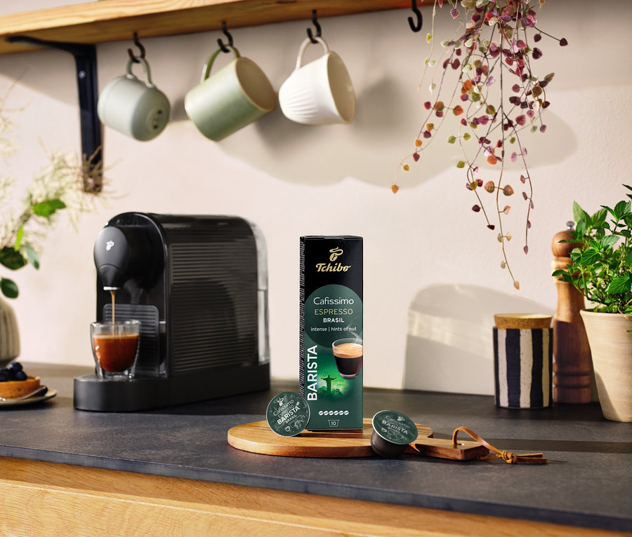 Siyah kahve makinesi, bir bardakta kahve hazırlıyor ve yanında Espresso Brasil – 10 Kapsül paketi bulunuyor.