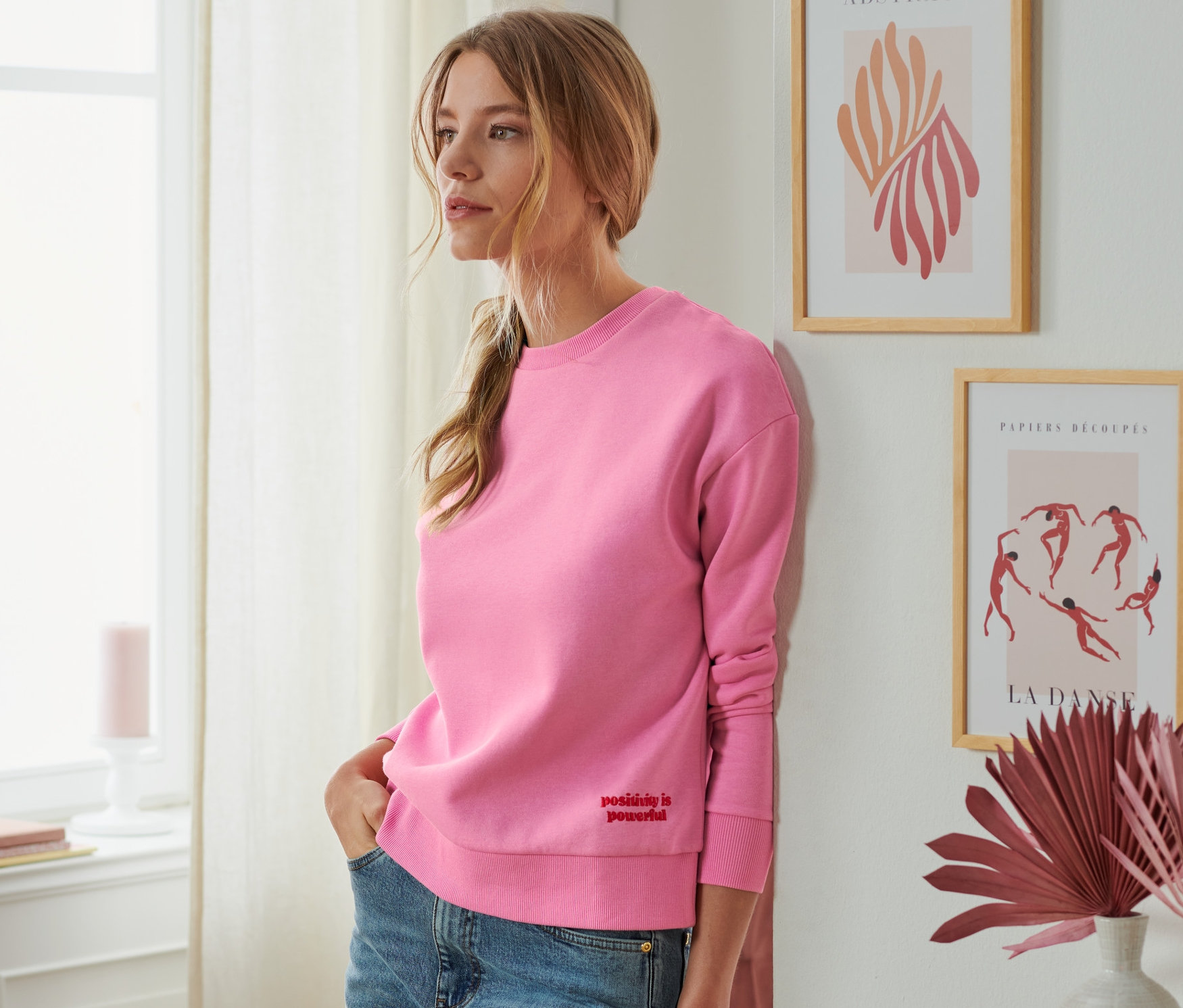 Duvara yaslanmış pembe sweatshirt giyen bir kadın.