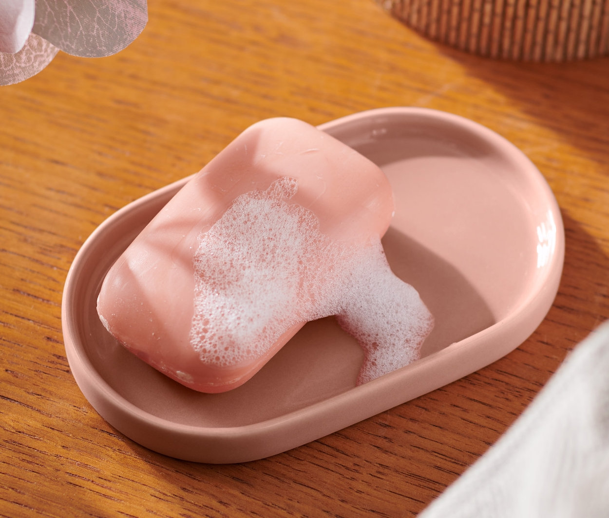 Pembe sabunluk içinde sabun, ahşap masa üzerinde orkide yanında duruyor.