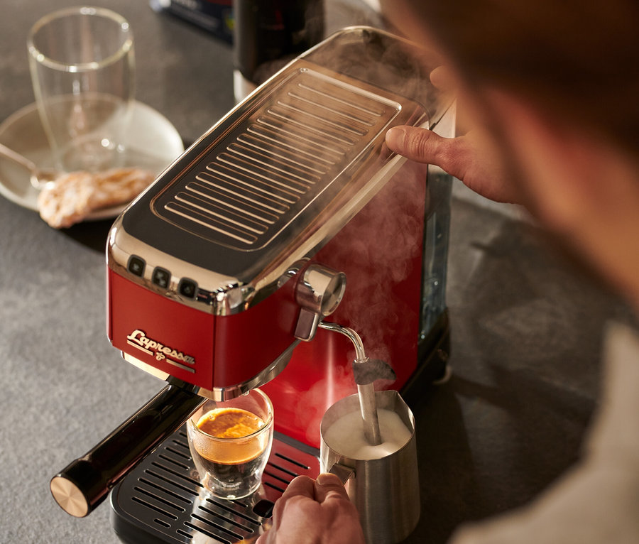 Adam, kırmızı »Lapressa« Portafiltre Makinesi ile kahve hazırlayıp süt köpürtüyor.