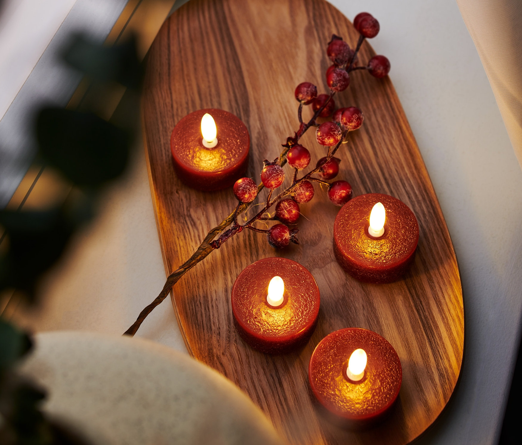 Kırmızı renkli 4 adet LED gerçek mum tealight, ahşap bir tepsi üzerinde kırmızı meyvelerden oluşan bir dal ile birlikte duruyor.