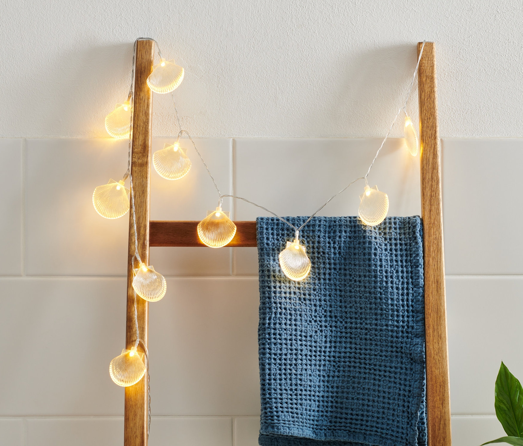 Midyeli LED ışık zinciri, üzerine mavi bir havlu asılmış ahşap bir merdivenden sarkıyor.
