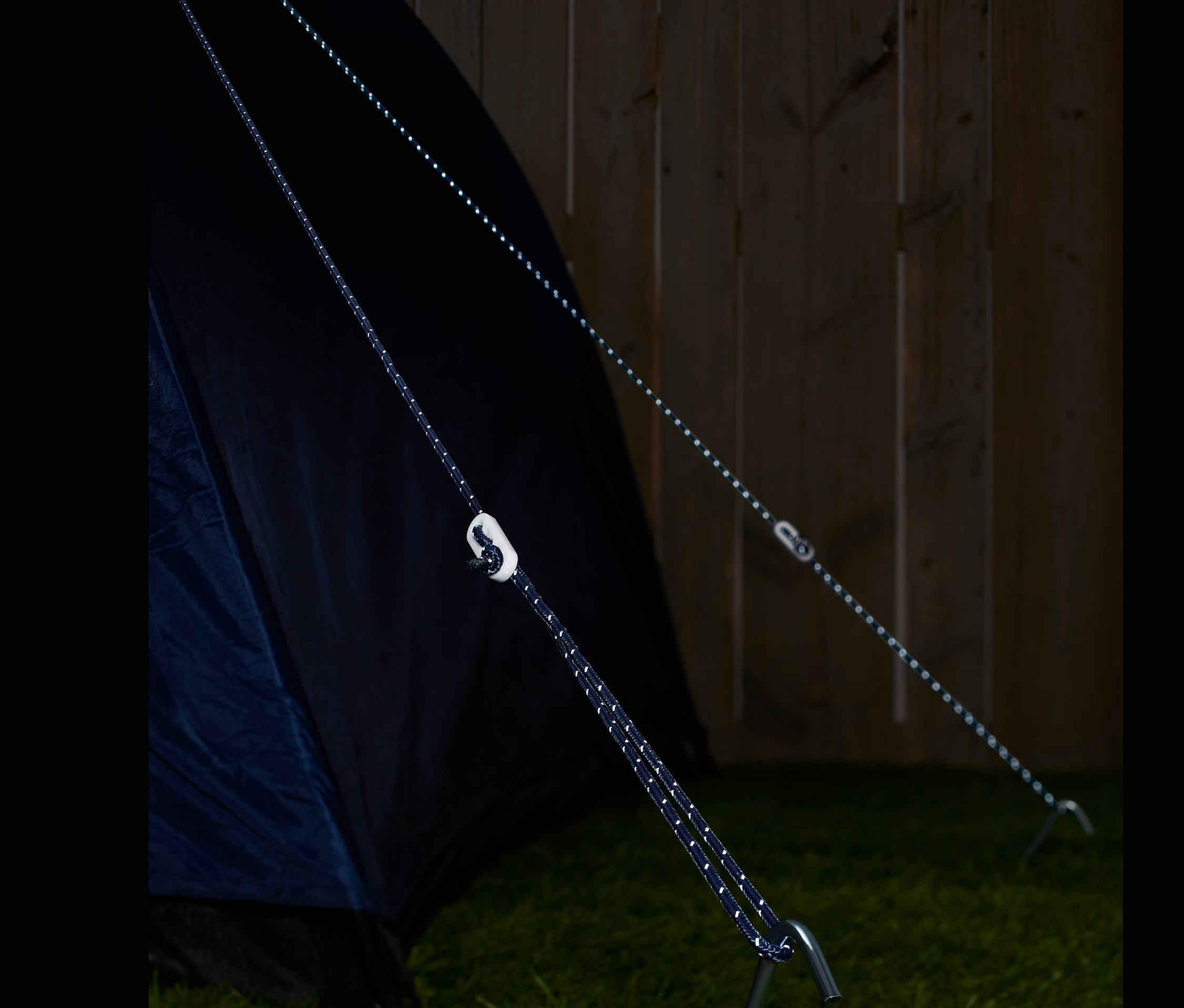 Çimde bir çadıra ve kazığa takılı iki adet reflektörlü gergi ipi.