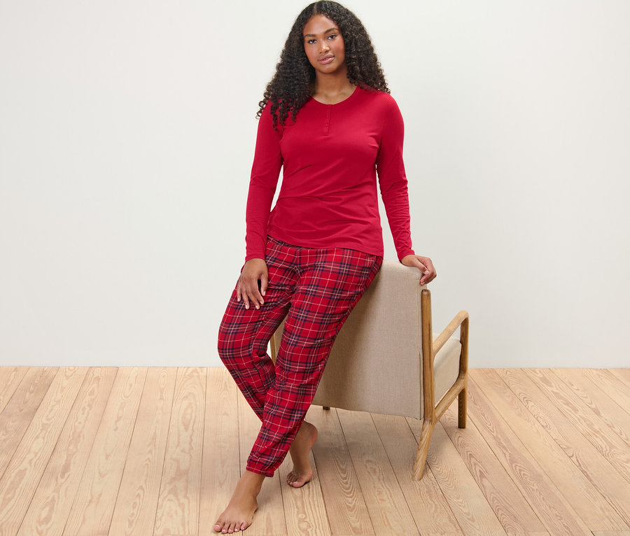 Bir kadın sandalyeye yaslanmış poz veriyor ve kareli pazen pijama takımı giyiyor.