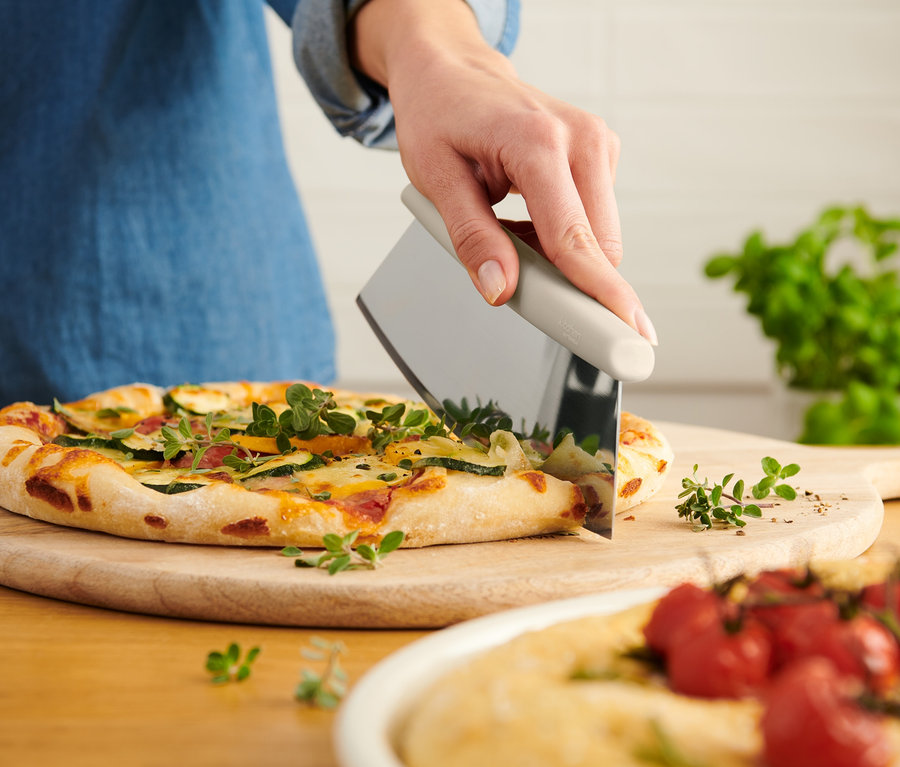 Kadın, Pizza ve Yeşillik Kesici ile pizza kesiyor.