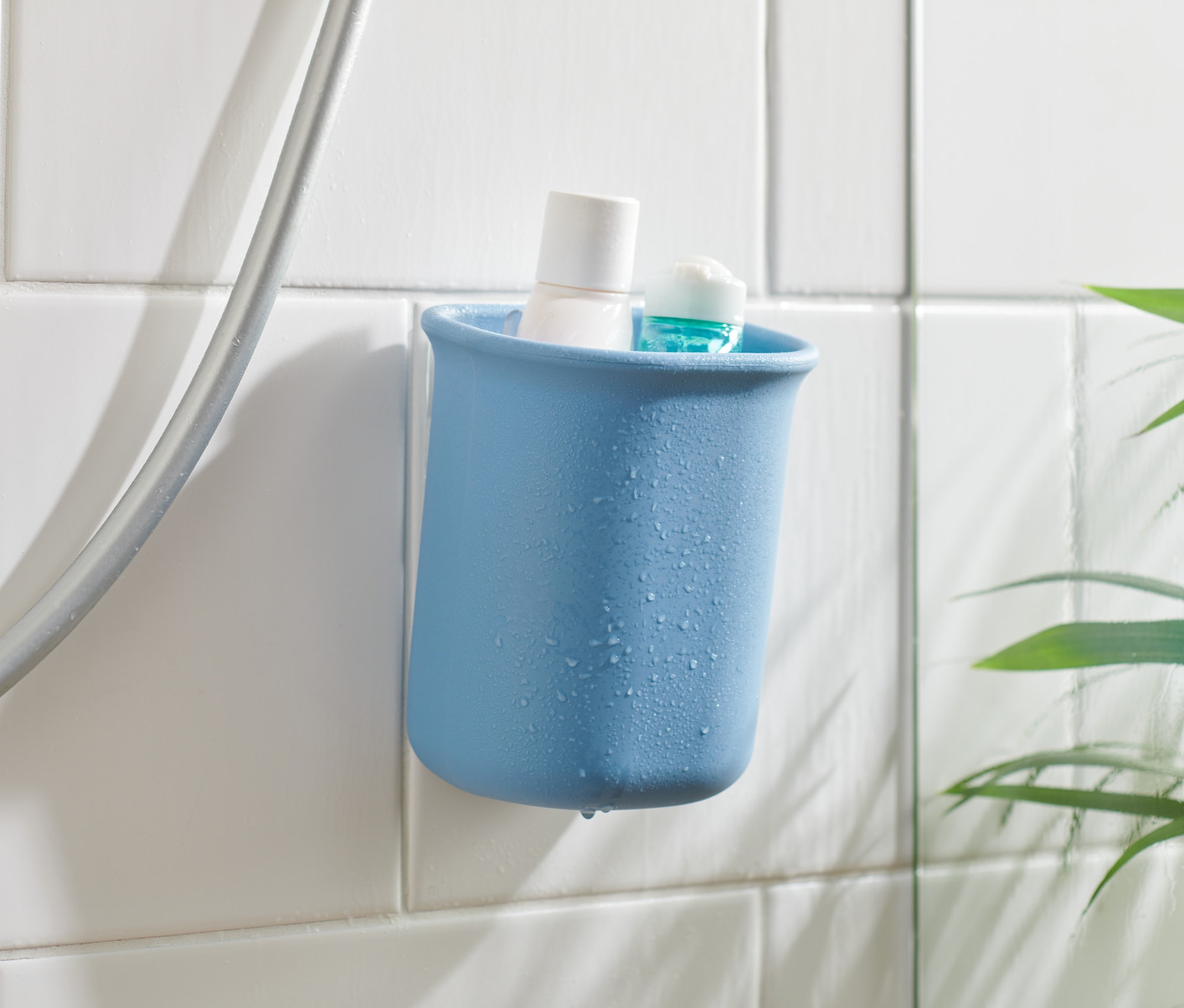 Duş hortumunun yanında beyaz fayanslara tutturulmuş, içinde beyaz ve mavi ürün bulunan mavi bir banyo düzenleme kabı.