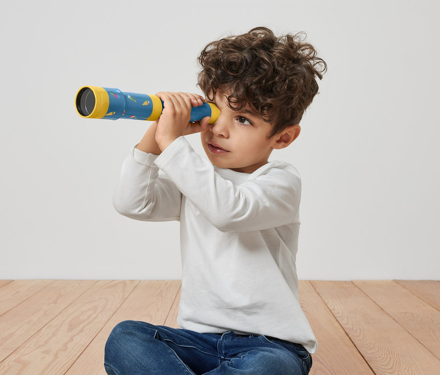 Oğlan yerde oturuyor ve oyuncak dürbün ile bakıyor.