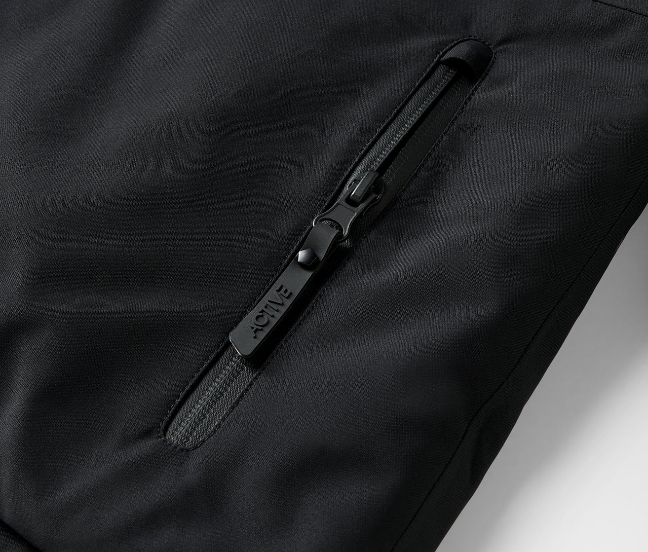 ACTIVE yazılı, siyah bir ceket fermuarının detayı.