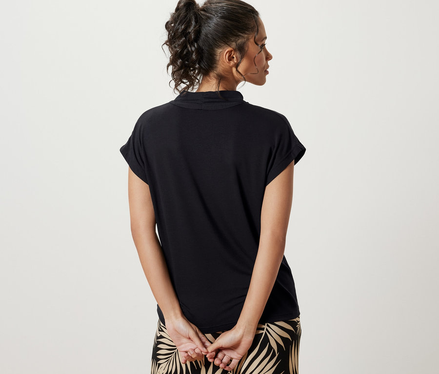 Arkası dönük bir kadın, siyah V yakalı bluz ve yaprak desenli bir pantolon giyiyor.