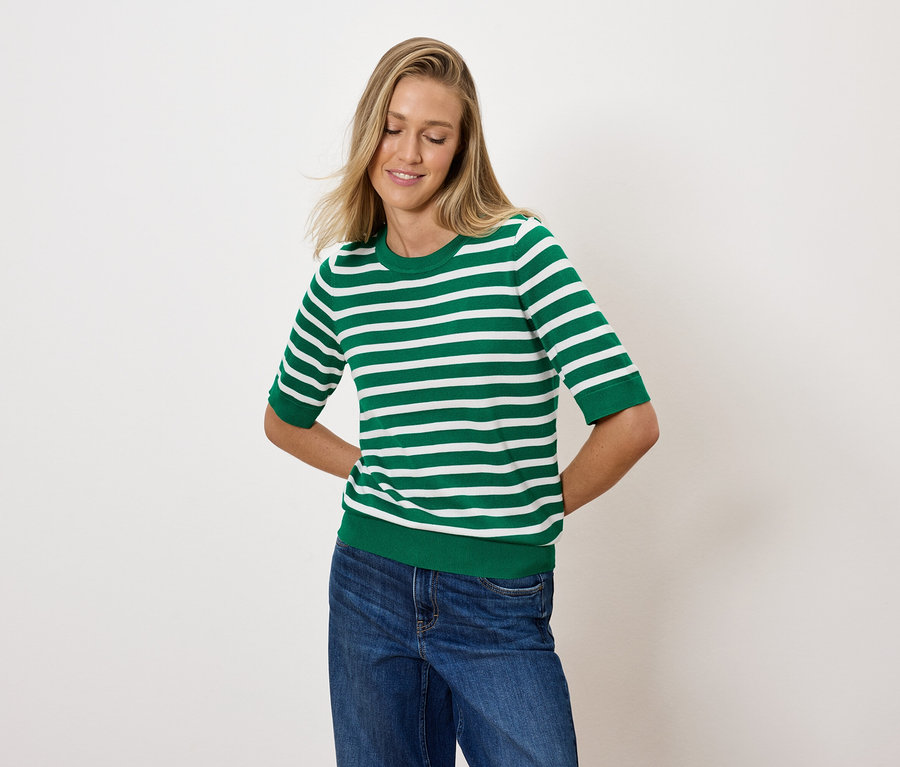 Sarışın bir kadın, yeşil beyaz çizgili bir üst ve mavi kot pantolonla poz veriyor.