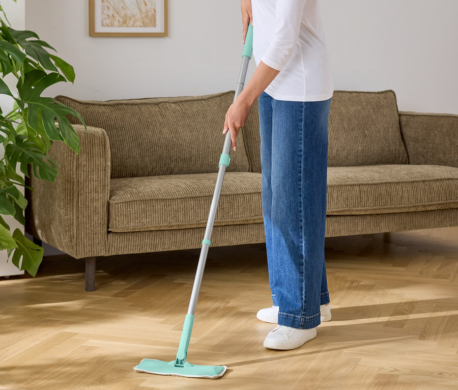 Kadın, turkuaz yeşili altlıklı bir paspasla ahşap zemini siliyor.