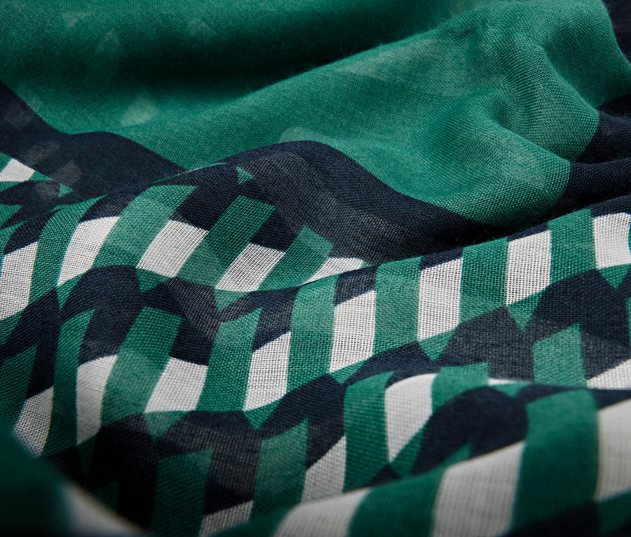 Koyu mavi zemin üzerine yeşil ve beyaz geometrik şekillerden oluşan bir desene sahip kumaşın yakın çekimi.