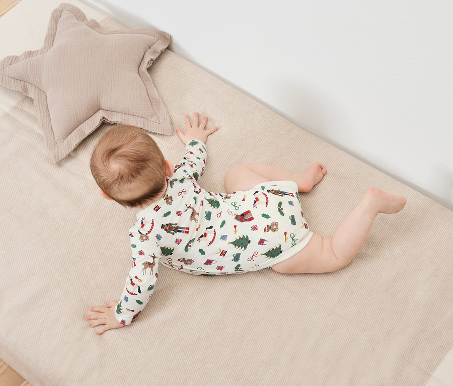 Bebek, bej yıldız şeklinde bir yastığın yanında, Noel desenli bir battaniyenin üzerinde yüzüstü yatıyor.