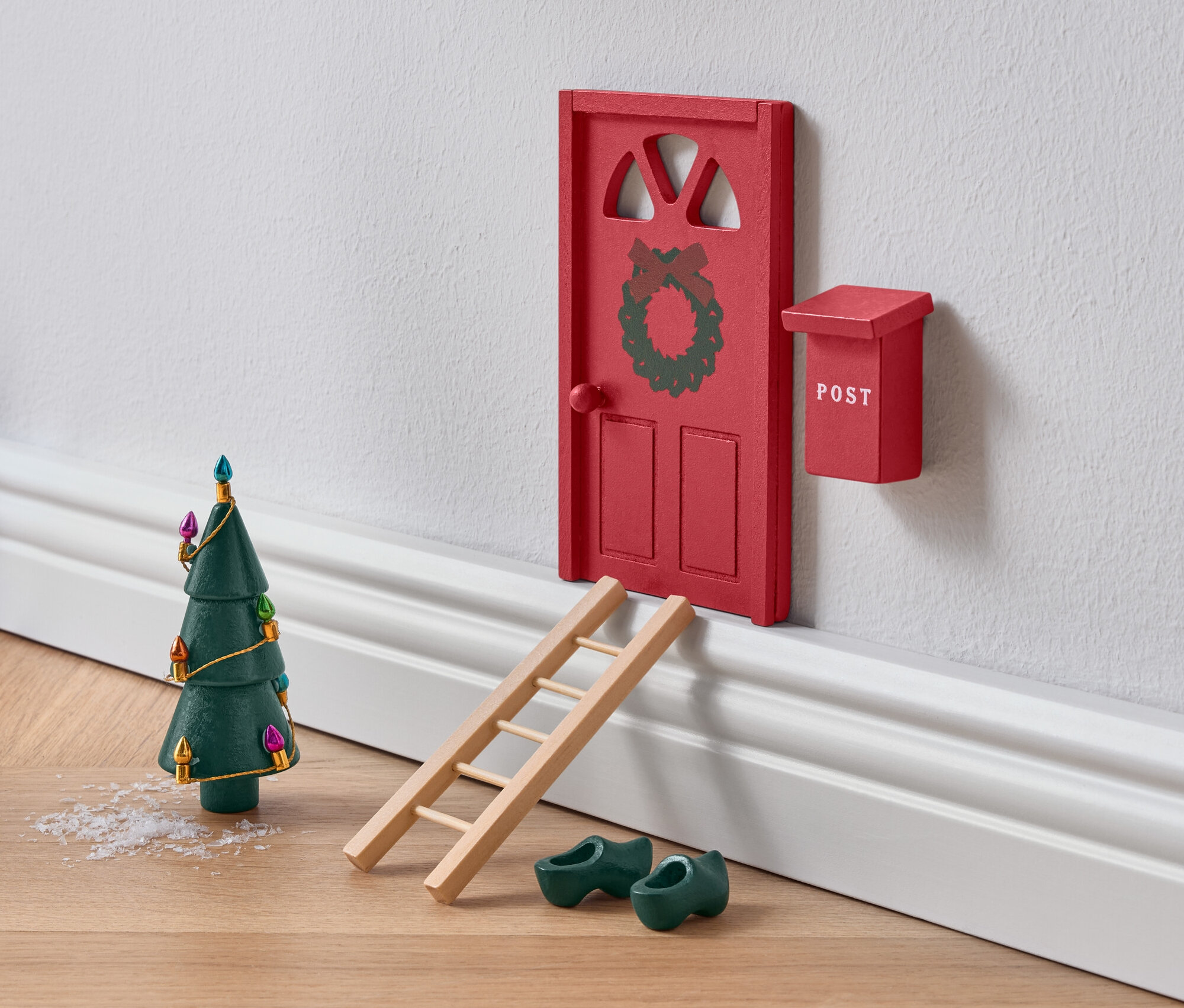 Çelenk, merdiven, yeşil tahta ayakkabılar ve Noel ağacı ile süslenmiş minyatür kırmızı kapı.