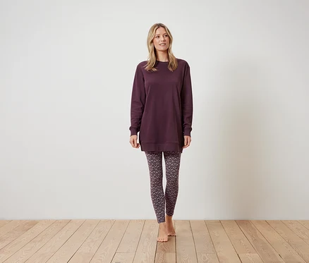 Kadın bordo bir sweatshirt ve desenli bir tayt giyiyor, ayakta duruyor.