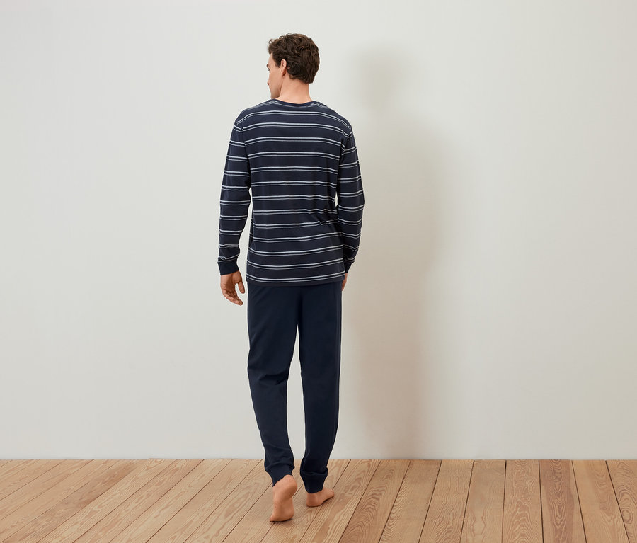 Çizgili pijamalı bir adam ahşap zeminde yalın ayak yürüyor.