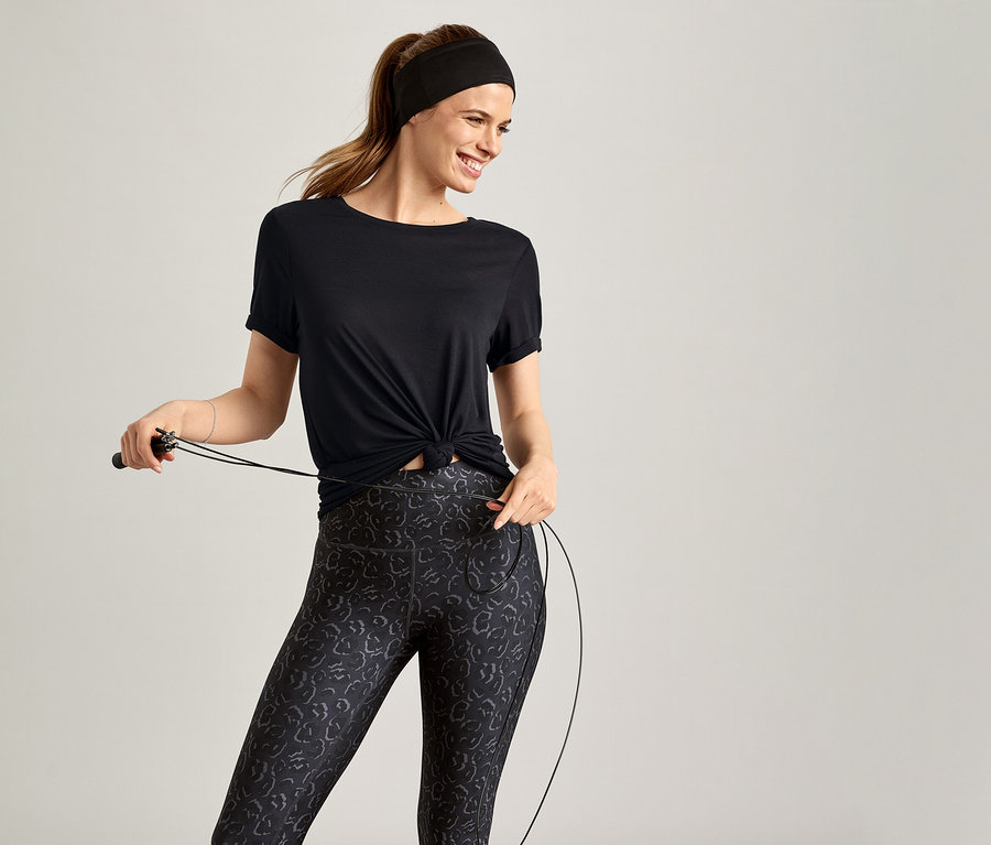 Siyah spor tişörtü giyen kadın gri fonda atlama ipi tutuyor.