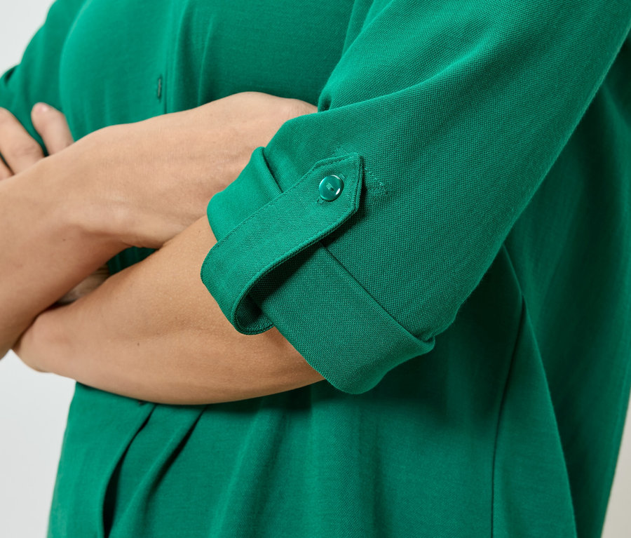 Kolları çaprazlanmış, düğmeli ve katlanmış kollu yeşil bir gömlek giyen bir kişinin yakın çekimi.
