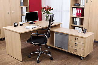 Açık renk ahşap ofis masası ve çeşitli ofis dolaplarının bulunduğu çalışma yeri.
