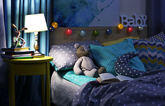 Genç bir anne, gece lambası yanarken, küçük çocuğu ile yatakta yatarak kitap okuyor.