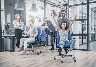 Beş genç çalışma arkadaşı, ofis koltuklarını ittirerek eğleniyor.