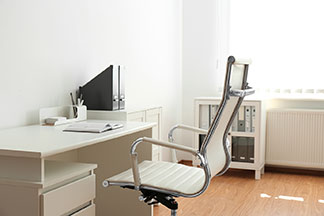 Beyaz döşemeli modern, ergonomik ofis sandalyesi beyaz bir ofis masasının önünde duruyor.