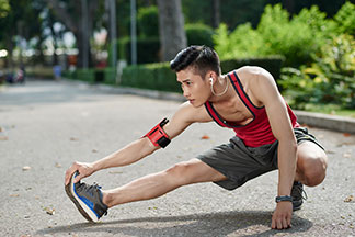 Spor giyimli ve spor ayakkabılı genç bir atletik adam bir parkta uzanıyor.