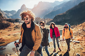 Outdoor kıyafetler giymiş gençlerden oluşan bir grup, dağlık bir bölgede yürüyüş yapıyor.