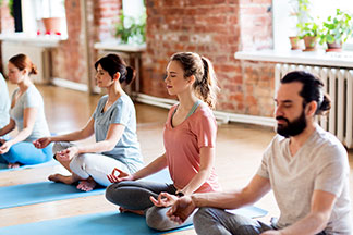 Doğru yoga giysisi: Bir grup genç, meditasyon yaparak, yoga matları üzerinde dizilmiş oturuyor.