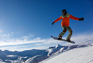 Kış için spor ceketler: Karlı dağlarda atlayış yapan bir snowboardcu.
